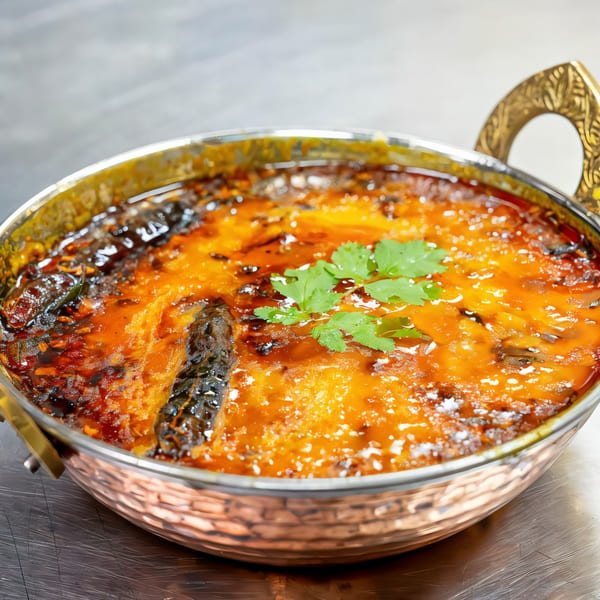 Indian dish in a copper serving bowl, garnished with fresh cilantro, on a metallic surface.