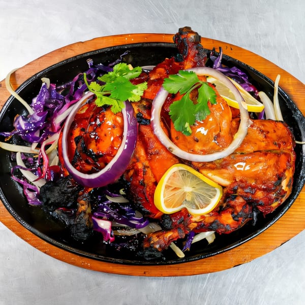 Indian Tandoori Chicken, garnished with red onions, cilantro, and lemon slices, served on a sizzling platter.
