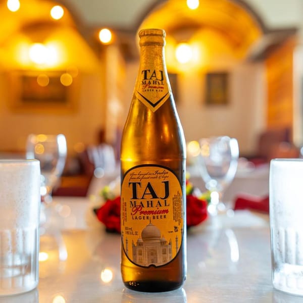 A bottle of Taj Mahal Premium Lager Beer on a table with glasses in an Indian restaurant.
