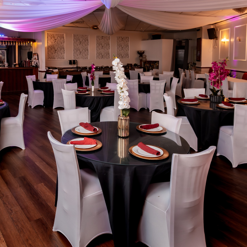 Elegant restaurant dining room with black-draped tables, white chair covers, red napkins, orchids, and purple ceiling drapery.