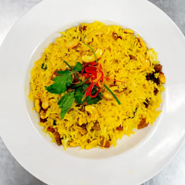Bright yellow Indian rice pilaf with cashews, raisins, and fresh herbs on a white plate.